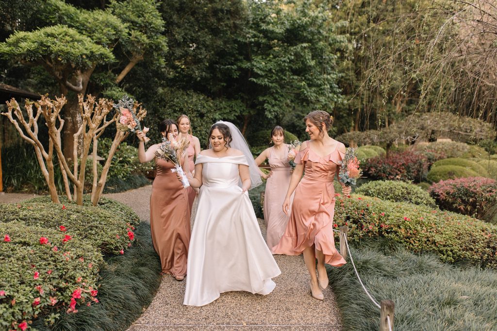 bridesmaids wearing different shades of soft pink and bride running through the garden