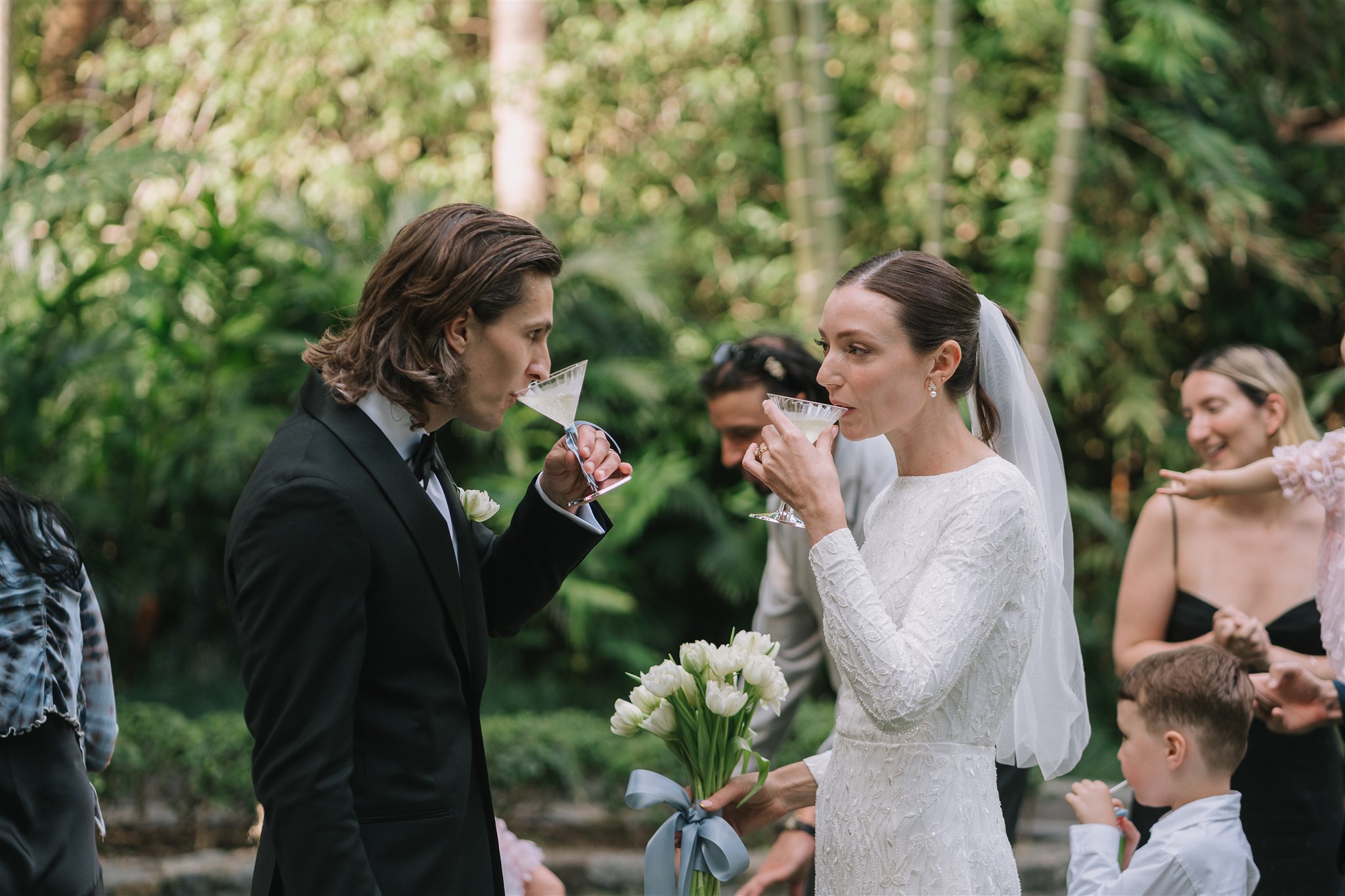 bride and groom facing each other sipping their wedding drinks from Champagne coupes with bride holding her bouquet with a blue ribbon
