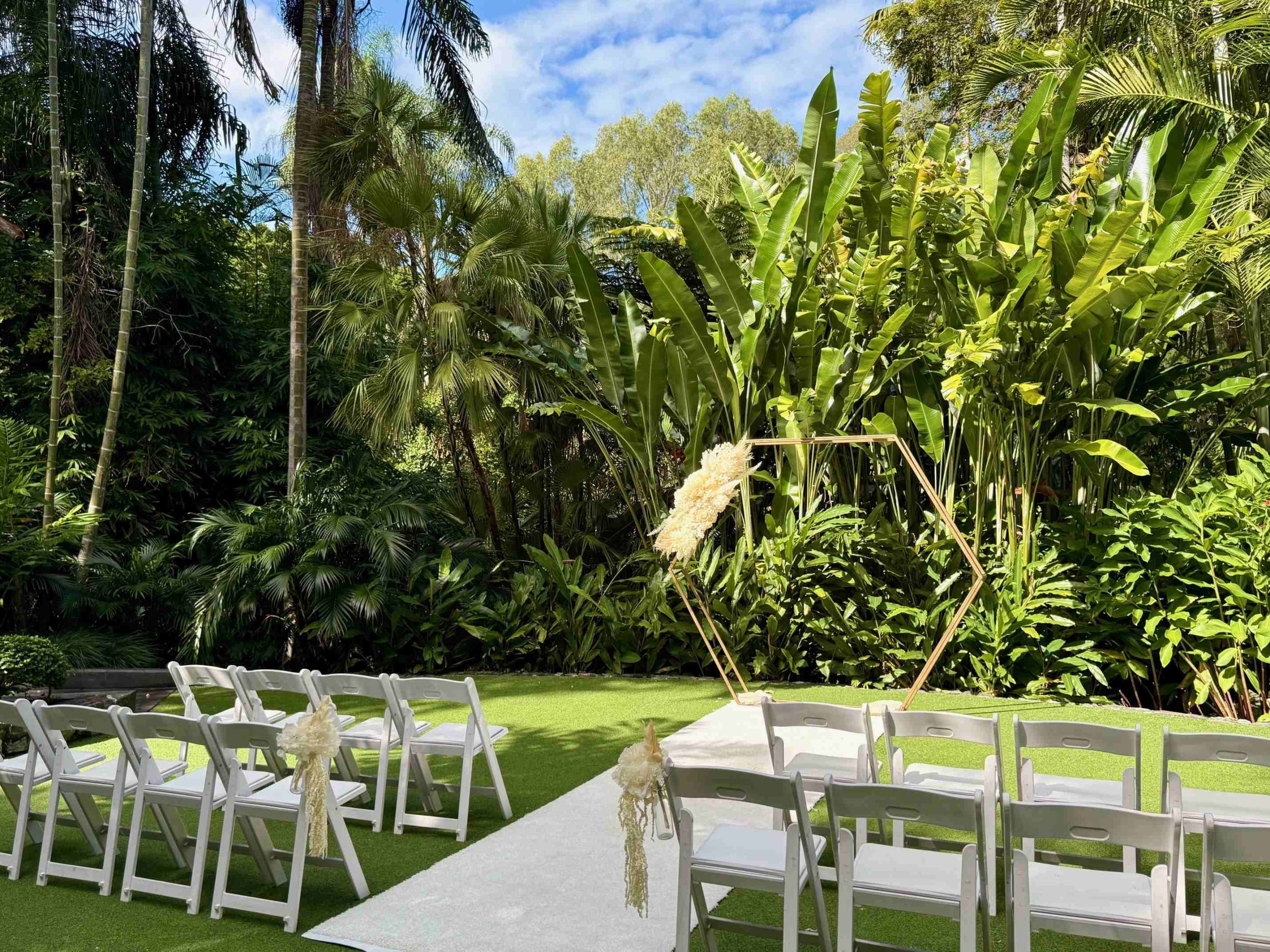 gold hexagonal wedding arch with tropical leaves in the backdrop with ivory dried floral arrangements at Palm Tree Lawn Mt Coot-tha Botanical gardens